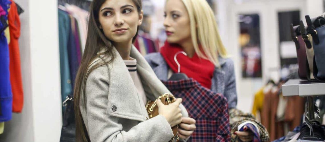 Two female friends shoplifting. Both about 20 years old in warm clothing, one blonde and one brunette.